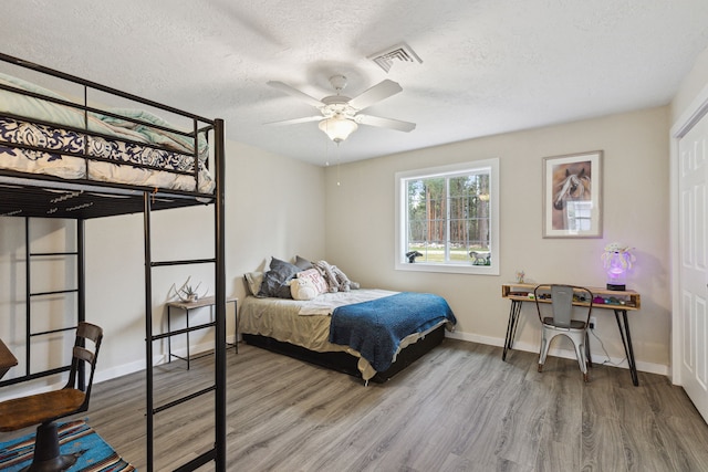 bedroom with a textured ceiling, wood finished floors, visible vents, and baseboards