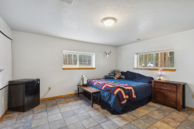 bedroom featuring a textured ceiling, refrigerator, visible vents, and baseboards