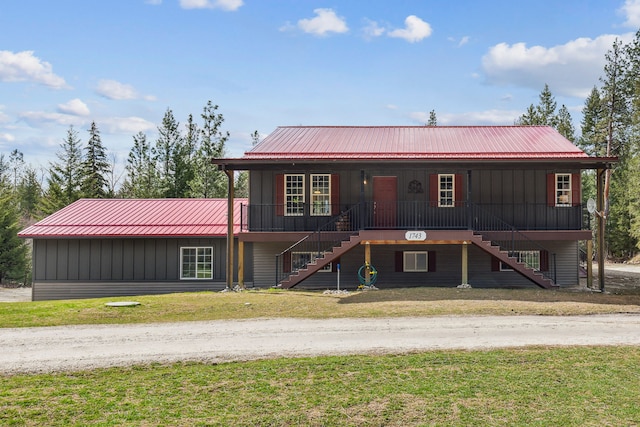 view of front facade with covered porch, board and batten siding, metal roof, a front lawn, and stairs