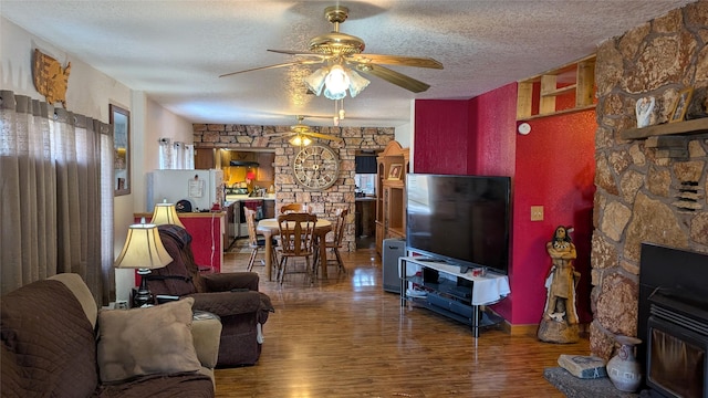 living area with ceiling fan, a fireplace, a textured ceiling, and wood finished floors