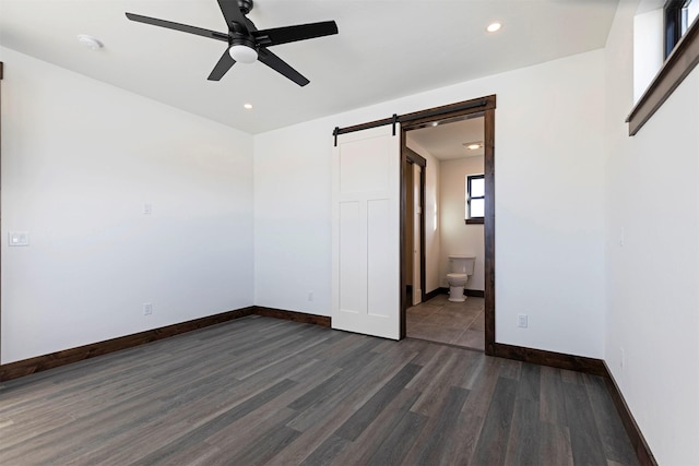 unfurnished bedroom featuring recessed lighting, ensuite bathroom, dark wood-type flooring, a barn door, and baseboards