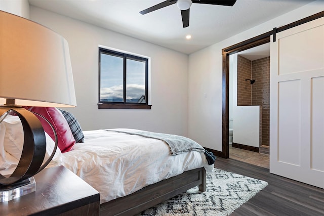 bedroom with recessed lighting, a barn door, dark wood-type flooring, a ceiling fan, and connected bathroom