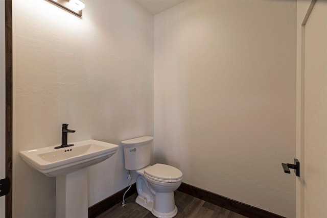 half bath with a sink, wood finished floors, toilet, and baseboards