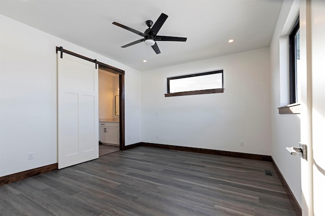 unfurnished bedroom with a barn door, visible vents, dark wood-style flooring, and baseboards