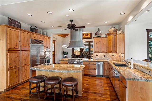 kitchen with light stone counters, island range hood, a peninsula, a sink, and appliances with stainless steel finishes