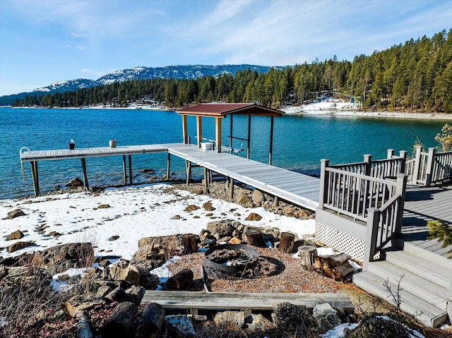 view of dock with an outdoor fire pit, a water view, and a view of trees