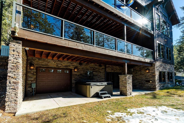 exterior space featuring an attached garage, stone siding, a hot tub, and driveway