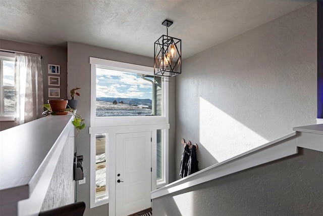 foyer entrance with a notable chandelier, a textured wall, and a textured ceiling