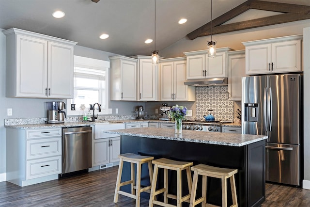 kitchen featuring appliances with stainless steel finishes, vaulted ceiling, a sink, a kitchen island, and under cabinet range hood