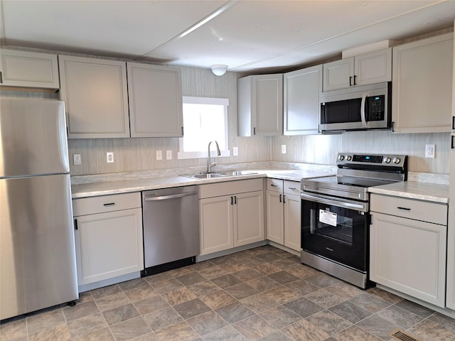 kitchen with a sink, light countertops, stone finish floor, and stainless steel appliances