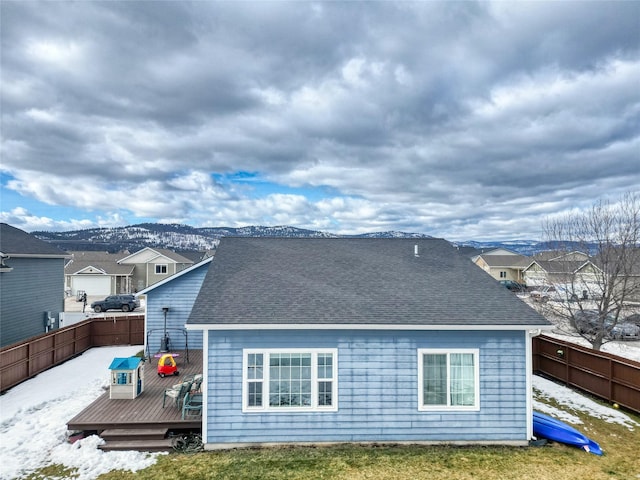 rear view of house with a deck with mountain view, a shingled roof, and fence