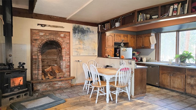 kitchen with brown cabinetry, light wood-style flooring, a wood stove, stainless steel dishwasher, and a sink