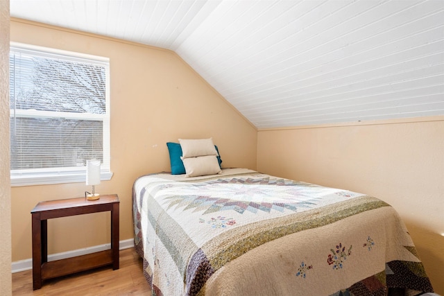 bedroom with vaulted ceiling, baseboards, and wood finished floors