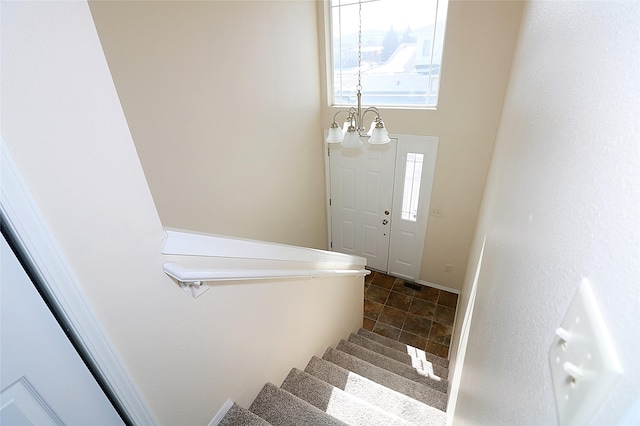 staircase featuring baseboards, stone finish floor, visible vents, and an inviting chandelier