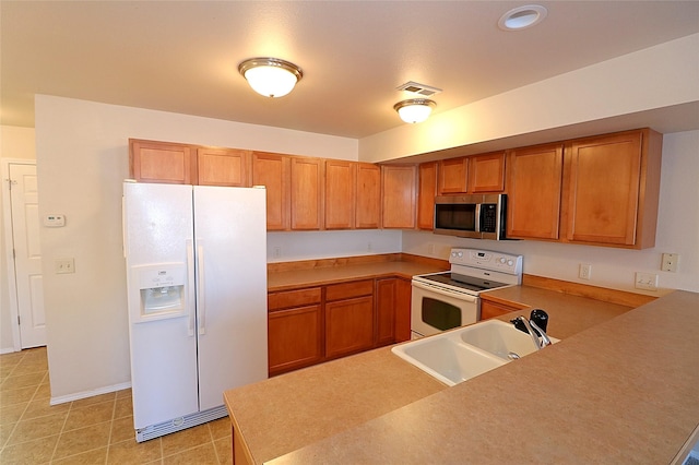 kitchen with white appliances, visible vents, brown cabinetry, and a sink