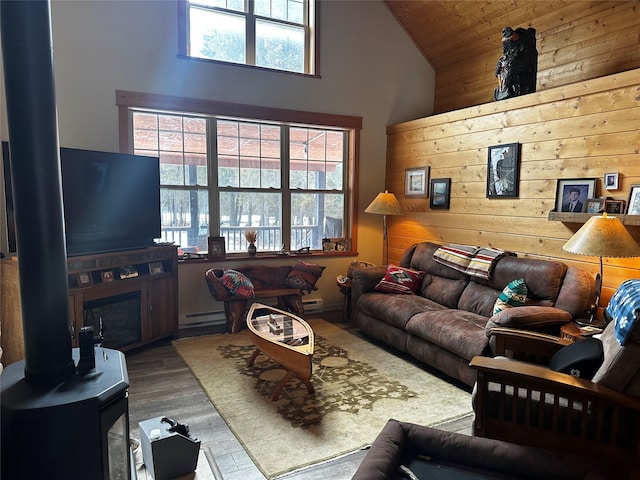 living area with high vaulted ceiling, a wood stove, wood walls, and wood finished floors