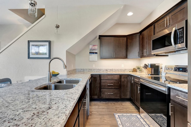 kitchen featuring appliances with stainless steel finishes, a sink, dark brown cabinetry, light stone countertops, and light wood-type flooring