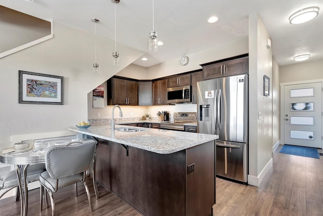 kitchen featuring stainless steel appliances, light wood-style floors, a sink, dark brown cabinets, and a peninsula