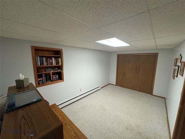 unfurnished office with carpet floors, built in shelves, baseboard heating, a drop ceiling, and baseboards