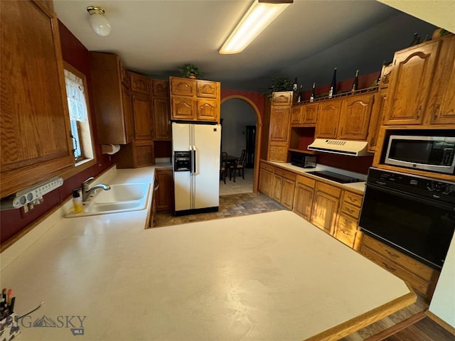 kitchen with arched walkways, light countertops, a sink, under cabinet range hood, and black appliances