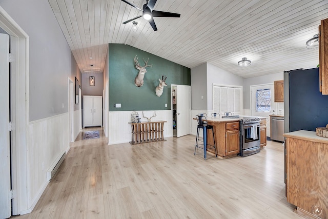 kitchen featuring lofted ceiling, a wainscoted wall, a baseboard heating unit, appliances with stainless steel finishes, and a kitchen bar