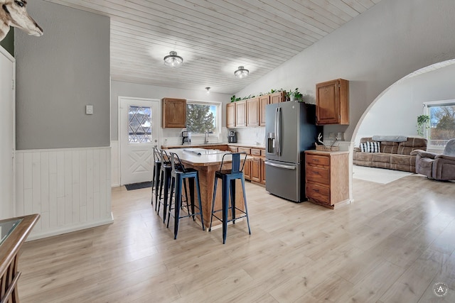 kitchen with arched walkways, a breakfast bar, a healthy amount of sunlight, and stainless steel refrigerator with ice dispenser