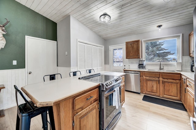 kitchen featuring wainscoting, lofted ceiling, wooden ceiling, stainless steel appliances, and a sink