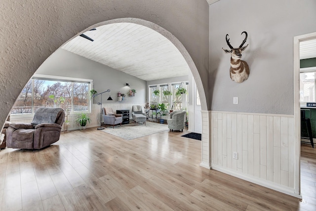 living area with arched walkways, a textured wall, lofted ceiling, wood finished floors, and wainscoting