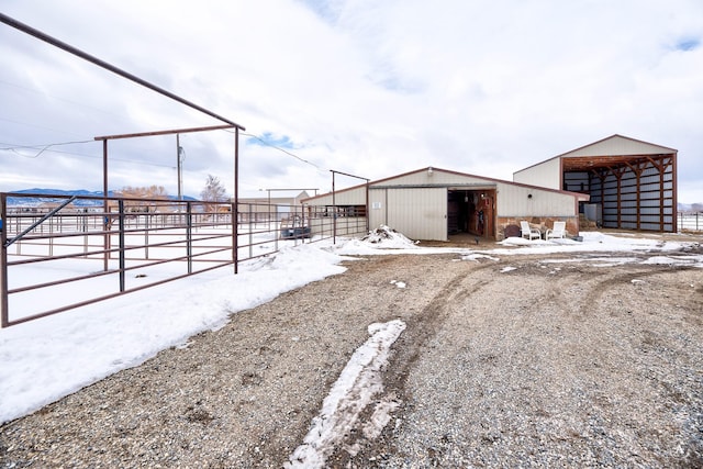 yard covered in snow featuring a pole building, an outdoor structure, an exterior structure, and a detached carport