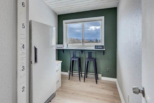 interior space featuring light wood-style floors, baseboards, a breakfast bar area, and a textured wall