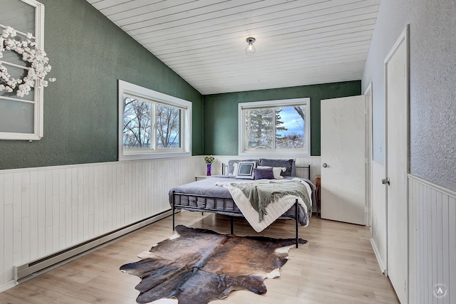 bedroom featuring a baseboard heating unit, lofted ceiling, a wainscoted wall, and wood finished floors