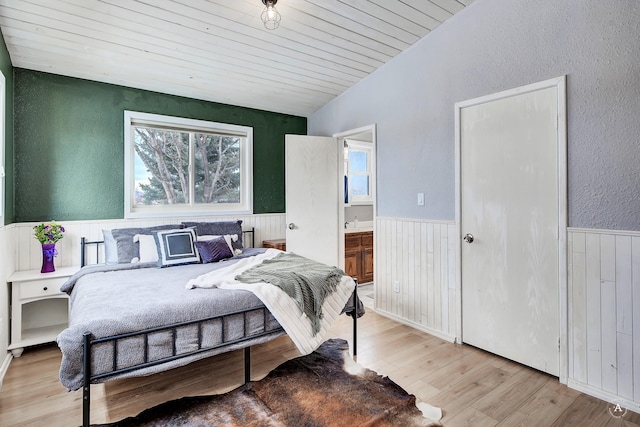 bedroom featuring light wood finished floors, wainscoting, connected bathroom, and wood ceiling