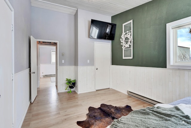 bedroom featuring a baseboard heating unit, a baseboard radiator, wainscoting, and light wood-style flooring