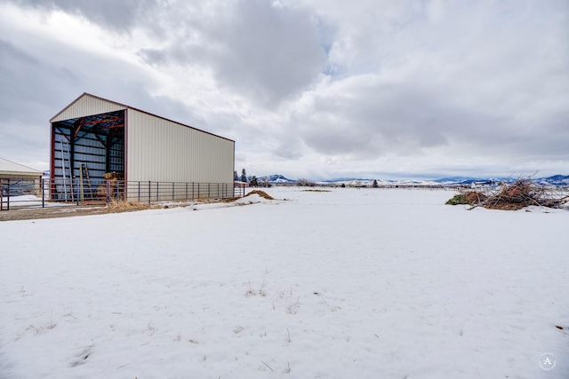 snowy yard featuring a pole building, an outdoor structure, and fence