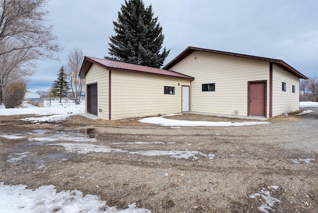 snow covered property with a detached garage, metal roof, and an outdoor structure