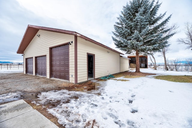 snow covered garage featuring a garage and fence