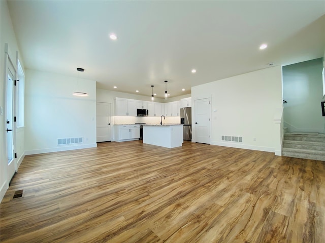 unfurnished living room with light wood-style floors, recessed lighting, stairs, baseboards, and a sink