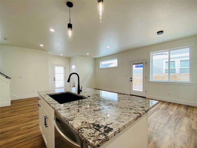 kitchen featuring wood finished floors, a sink, baseboards, stainless steel dishwasher, and pendant lighting