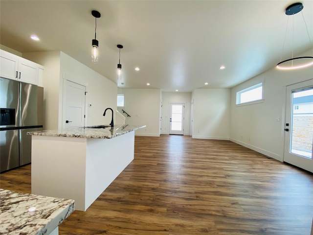 kitchen featuring stainless steel fridge, dark wood finished floors, light stone counters, hanging light fixtures, and a sink