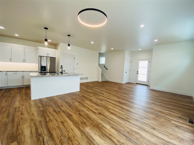 kitchen featuring visible vents, decorative backsplash, stainless steel fridge with ice dispenser, an island with sink, and wood finished floors