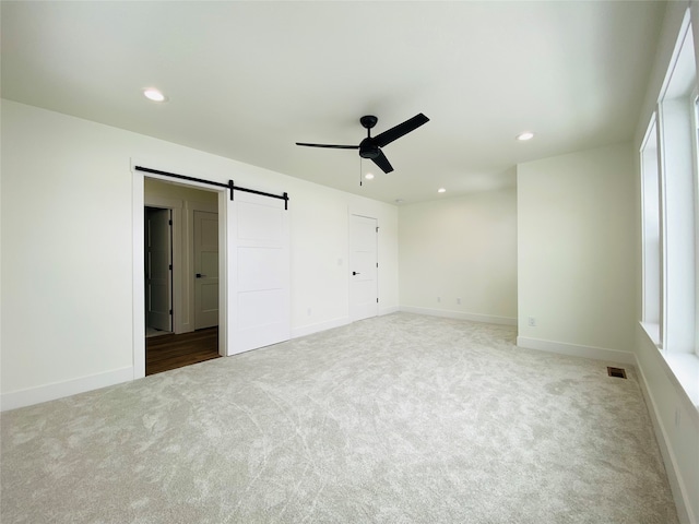 unfurnished bedroom featuring a barn door, recessed lighting, carpet floors, visible vents, and baseboards