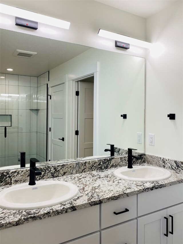 bathroom featuring visible vents, a sink, a shower stall, and double vanity