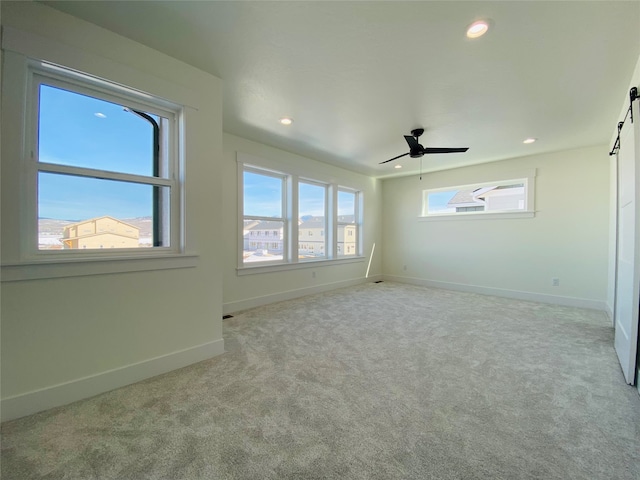 carpeted spare room featuring a barn door, baseboards, a ceiling fan, and recessed lighting