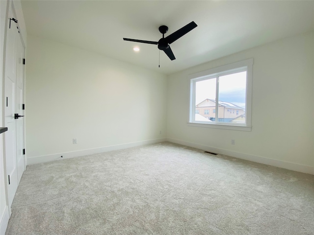 spare room with a ceiling fan, visible vents, light carpet, and baseboards