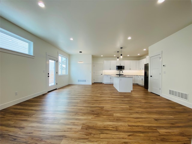 kitchen featuring stainless steel microwave, open floor plan, recessed lighting, a kitchen island with sink, and white cabinetry