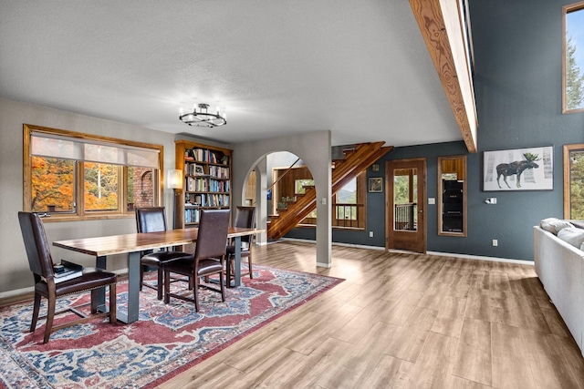 dining room with baseboards, arched walkways, wood finished floors, stairs, and beam ceiling