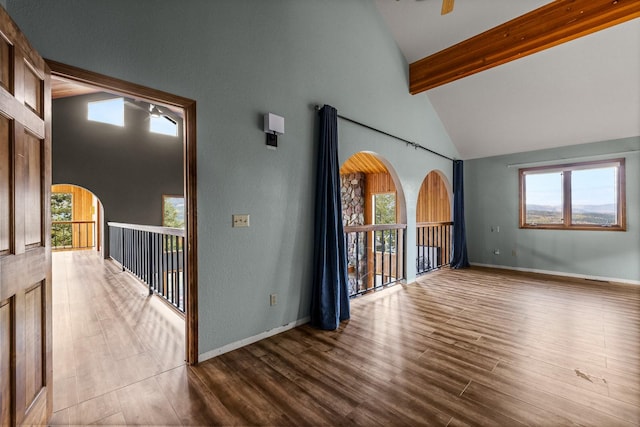 unfurnished room with arched walkways, beam ceiling, wood finished floors, high vaulted ceiling, and baseboards