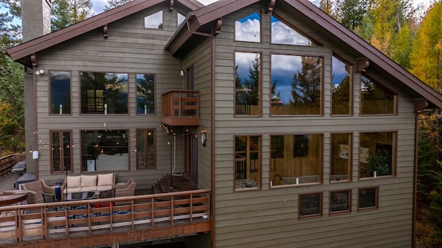 rear view of house featuring a chimney, a wooden deck, an outdoor living space, and a balcony