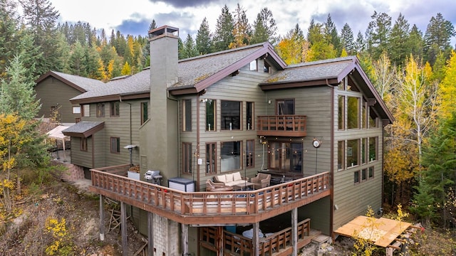 back of house featuring a shingled roof, a chimney, an outdoor hangout area, and a wooden deck