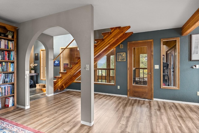 interior space with stairs, arched walkways, wood finished floors, and baseboards